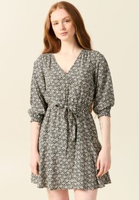 Svart blommig klänning med v-ringning, puffärmar, rynkad midja och knytbälte. Har ett mönster av små vita blommor på en mörk bakgrund.