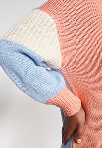 Sweter dziany o luźnym kroju, w pastelowych kolorach: brzoskwiniowym, kremowym i błękitnym. Teksturowane ściągacze i luźne rękawy.