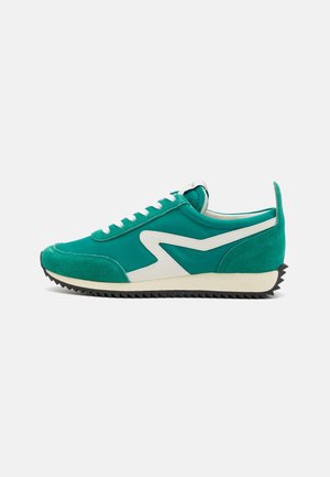 Sneaker med lav profil i blågrøn med hvid zigzag-side-stribe, hvide snørebånd, tekstureret sort sål og ruskind detaljer ved tåen og hælen.