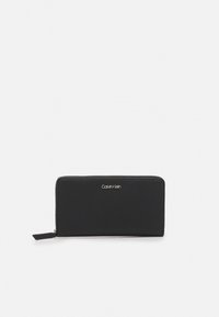 Portefeuille en cuir noir Calvin Klein, fermeture à glissière, forme rectangulaire, texture lisse, avec un logo minimaliste à l'avant.