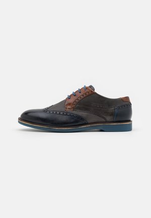 Chaussure brogues homme en cuir noir et marron avec lacets et semelle bleus, présentant des perforations décoratives et des panneaux texturés.