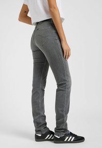Grijze denim skinny jeans met een middelhoge tailleband, voorzien van ton-sur-ton stiksels en achterzakken. Gepaard met zwarte sneakers met witte strepen.