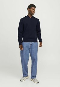 Felpa con cappuccio blu navy a maniche lunghe, abbinata a jeans larghi azzurri e sneakers grigie. Tessuto morbido, vestibilità casual e design semplice.