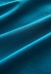 Tissu de coton bleu sarcelle avec une texture lisse et douce, présentant des plis légers et un éclat subtil, mettant en valeur sa couleur uniforme et vibrante.