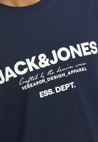 Camiseta de algodón azul marino con texto en blanco en negrita: "JACK & JONES", y texto más pequeño con varias frases, escote redondo, textura suave.