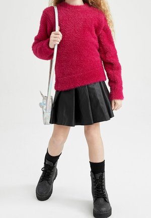 Barn iført en fluffy rød sweater, sort plisseret nederdel, sorte snørebåndsstøvler og holder en skinnende sølv skuldertaske.