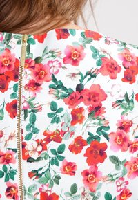 Weißes Blumenkleid mit einem lebhaften roten Blumenmuster und grünen Blättern. Auffälliger goldener Reißverschluss hinten. Glatte Stofftextur.