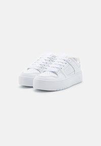 Weiße Sneakers aus synthetischem Material mit flachem Schuhsohle, runder Zehenform und flachen Schnürsenkeln. Leichte Textur mit durchbrochenen Details.