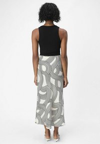 Sort ribbet tanktop bæres med en svævende midi-skort, der har en hvid bund og dristige sorte bølgede linjemønstre. Glat tekstur, enkel design.