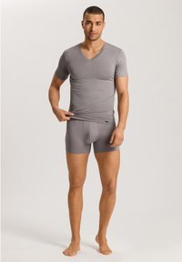 T-shirt grigia a scollo a V e pantaloni boxer, realizzati in un tessuto morbido. La maglietta ha maniche corte e una vestibilità aderente, con un'etichetta logo sulla cintura.