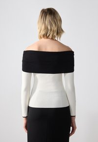 Off-the-shoulder top with a black ribbed neckline and long white sleeves, fitted silhouette, and smooth fabric texture.