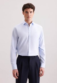 Camicia button-up azzurra chiara con taschino sul petto, maniche lunghe e una texture liscia, abbinata a pantaloni plissettati scuri.