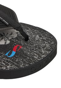 Chanclas negras con una plantilla texturizada que presenta un patrón desgastado y un logo multicolor. La correa trenzada añade durabilidad y agarre.