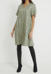 Kortärmad, knälång klänning i grön med ett geometriskt mönster av trianglar i marinblått och krämfärgat. V-ringad design, lättviktigt tyg.