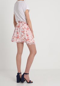 Jupe florale rose clair avec une taille froncée. Présente de petits motifs floraux de différentes couleurs. Associée à des sandales à talons carrés bleu marine.