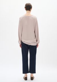 Blusa viola chiaro a maniche lunghe, con polsini elasticizzati e scollatura rotonda, abbinata a pantaloni in denim blu scuro e scarpe con stampa animalier.