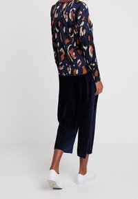 Marinblå mönstrad långärmad topp med orange och vita abstrakta mönster, matchad med strukturerade svarta culotter och vita sneakers.