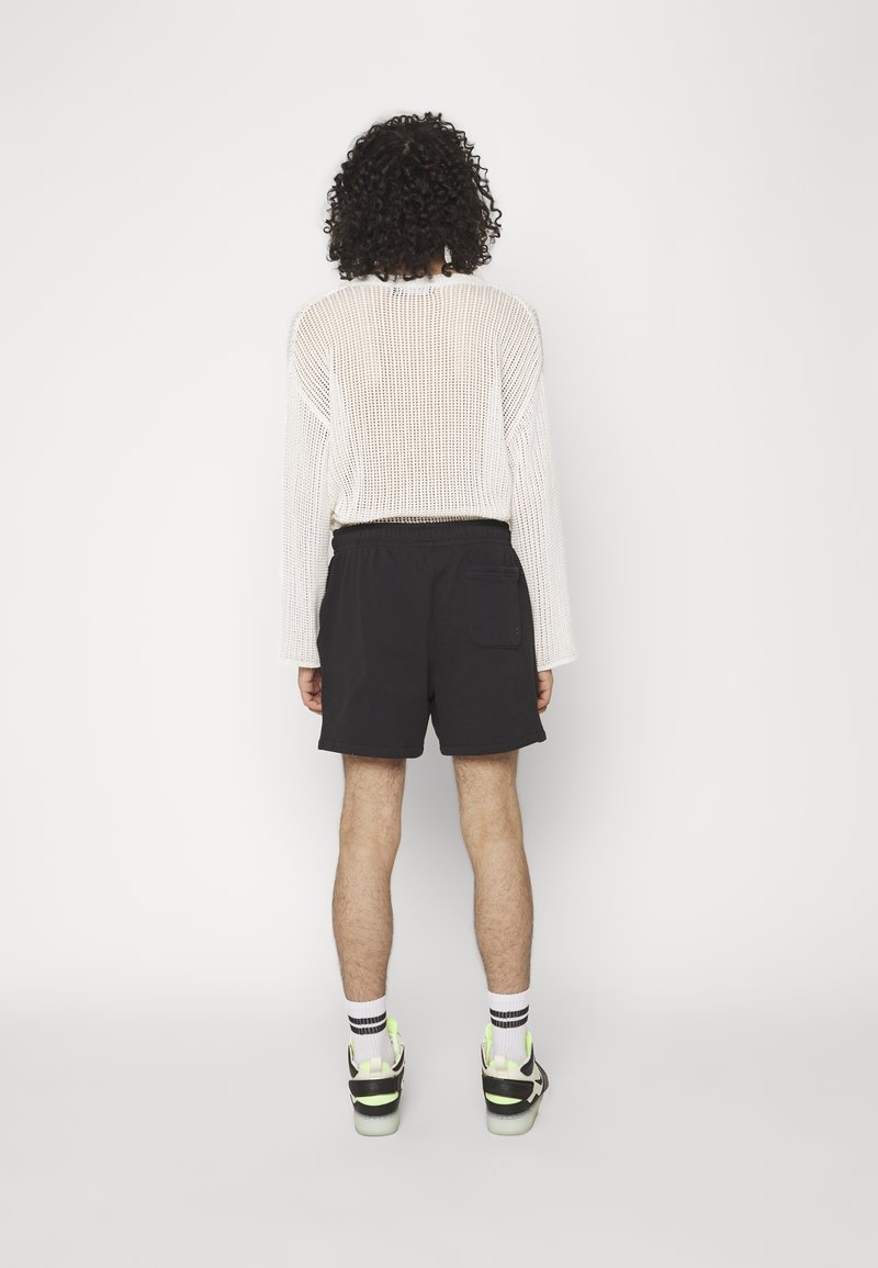 Vit mesh långärmad tröja, svarta shorts med elastisk midja och svarta sneakers med neonlysande detaljer. Texturerad och avslappnad design.