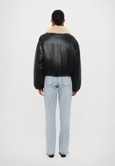 Veste bomber en cuir noir avec un col en fausse fourrure beige, des manches bouffantes et une coupe courte, associée à un jean taille haute bleu clair.