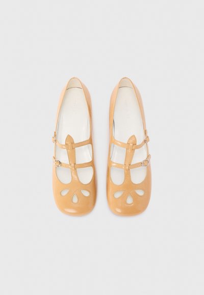 Ballet flat in pelle tan con motivo floreale ritagliato, due cinturini regolabili e finitura lucida. Punta arrotondata e suola piatta. Nessun marchio visibile.