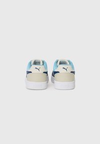 Sneaker Puma con parte superiore blu chiaro e navy, dettagli beige e suola in gomma bianca. Presenta il logo sul tallone e una texture liscia.