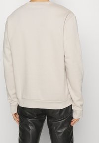 Světlé béžové triko s kulatým výstřihem, žebrovanými manžetami a lemem. Měkká textura, klasický střih, ve spojení s černými lesklými kalhotami.