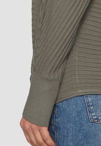 Gray ribbed long-sleeve top featuring a textured design and fitted cuffs, paired with blue denim jeans.