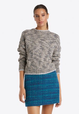 Flauschiger Strickpullover in Grautönen mit rundem Ausschnitt, getragen mit einem strukturierten blauen Minirock, der ein gewebtes Muster zeigt.
