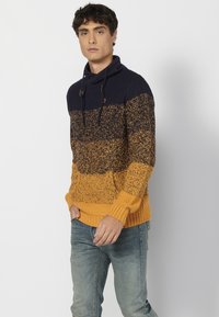 Suéter de punto con un diseño en degradado de azul marino y mostaza, con un cuello alto, bolsillo delantero y puños y dobladillo acanalados.