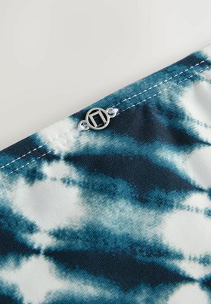Textiel met een blauw-wit tie-dye patroon, voorzien van een zilveren logo accent en contrasterende stiksels langs de rand.