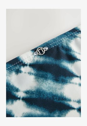 Tekstil med et blåt og hvidt tie-dye mønster med et sølvlogo som accent og kontraststing langs kanten.