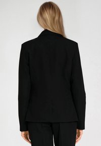 Czarna marynarka o dopasowanym kroju, z pojedynczym rozcięciem z tyłu, klapami wyciętymi w szpic i długimi rękawami. Gładka tekstura materiału, minimalistyczny design.