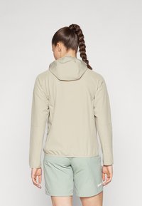 Veste légère beige avec capuche, présentant une texture lisse et des poignets élastiques, associée à un short vert menthe. Vue de dos.