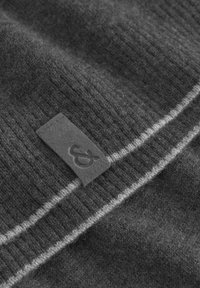 Weiches, dunkelgraues Strickgewebe mit gerippter Textur, das mit einem kleinen rechteckigen Etikett versehen ist, auf dem ein Und-Zeichen geprägt ist.