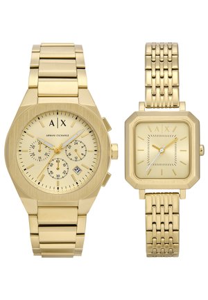 Montre en ton or comprenant un boîtier octogonal épais avec des cadrans chronographes et une montre à bracelet en maille rectangulaire. Les deux ont des designs minimalistes.