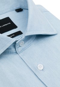 Jasnoniebieska koszula zapinana na guziki, uszyta z miękkiego materiału, cechująca się slim fit, ostro zakończonym kołnierzykiem i białymi guzikami. Metka jest widoczna na kołnierzyku.