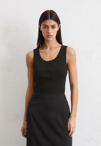Top negro de canalé con escote en forma de lágrima y detalle de tres botones en la parte delantera, combinado con una falda negra a juego.