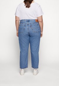 Jeans de mezclilla azul de cintura alta con un ajuste holgado, dobladillos acabados y una etiqueta de cuero en la cintura trasera. Camiseta blanca y zapatillas visibles.