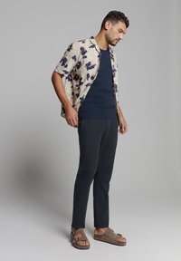 Bloemig shirt met korte mouwen in crème met marineblauwe bloemen, gecombineerd met een donker marineblauw getailleerd topje, slanke donkere broek en bruine sandalen met banden.