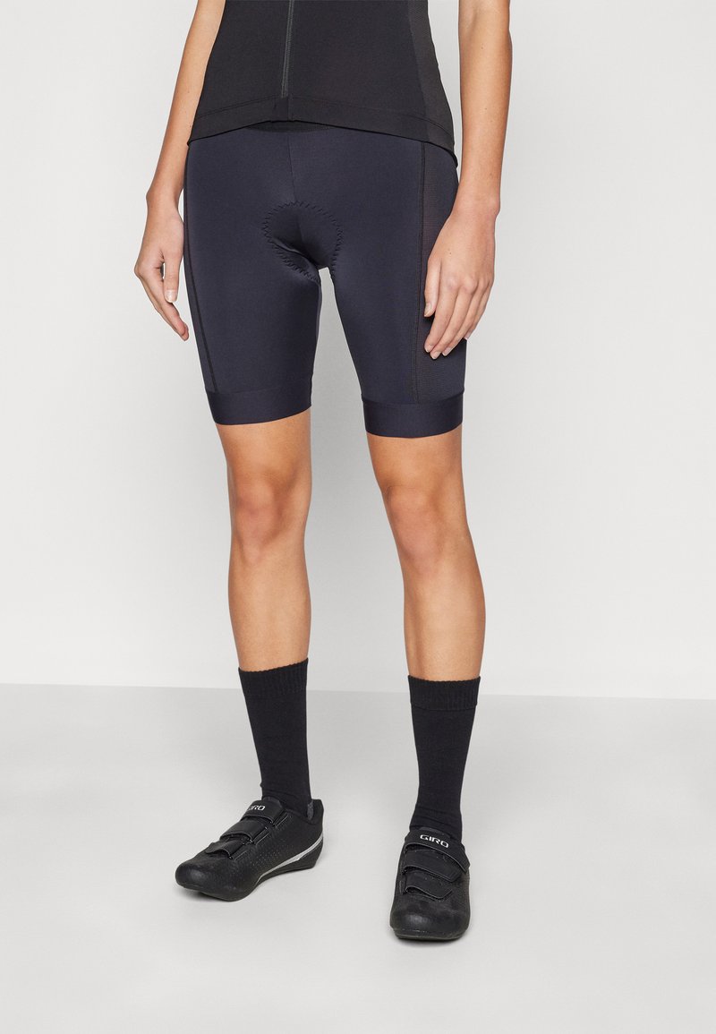 Schwarze Radshorts mit gepolstertem Einsatz, aus dehnbarem Stoff, mit kontrastierenden strukturierten Seiten, sowie passenden schwarzen Socken und Schuhen.