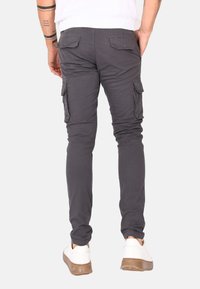 Pantaloni cargo grigi con vestibilità slim, tessuto elasticizzato e tasche laterali. Presentano tasche posteriori e una texture liscia, abbinati a sneakers bianche.