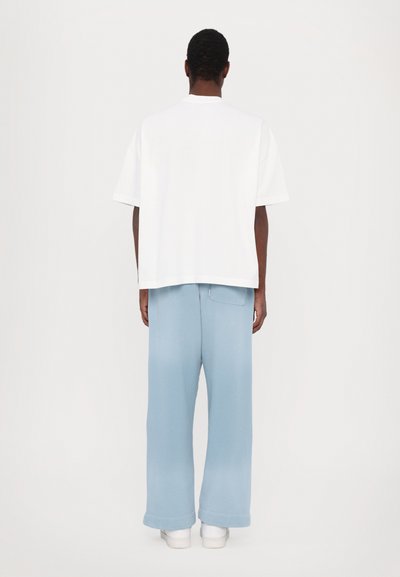 T-shirt en coton blanc à coupe ample avec des manches courtes, associé à un pantalon bleu clair à coupe décontractée avec un dégradé de couleur.