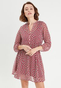 Robe chemise à carreaux rouges et blancs avec un motif tourbillonnant, devant à boutons, manches longues et tissu léger et fluide.
