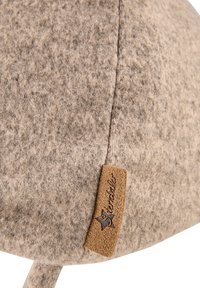 Brown felt hat with a rounded shape, featuring a textured surface and a tan leather tag with embossed branding on the side.