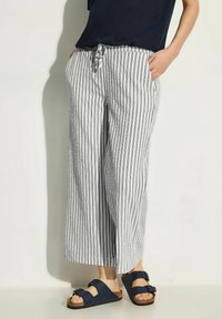 Striped coastal pants in white and navy, loose fit, mid-rise with drawstring waist, featuring two side pockets. Worn with dark sandals.