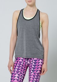 Canotta atletica grigia con bordo nero indossata su uno strato giallo chiaro, abbinata a leggings multicolori con motivo geometrico rosa e viola.