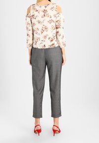 Blouse crème à motifs floraux avec des épaules dénudées ; associée à un pantalon à carreaux gris taille haute et des sandales à talons rouges.