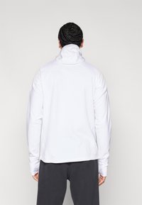 Fehér pulóver kapucnis felső magas gallérral és hosszú ujjakkal. Simogató tapintású, testhez simuló fazonú, látható logók vagy minták nélkül.