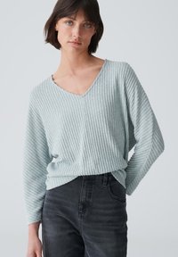 Hellblauer gerippter Strickpullover mit V-Ausschnitt und langen Ärmeln, kombiniert mit schwarzen Jeans. Weicher Stoff und lockere Passform.