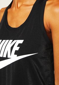Černý bezrukávový top vyrobený z hladkého materiálu, který obsahuje výrazné bílé logo "NIKE" a zakřivený design swoosh přes trup.